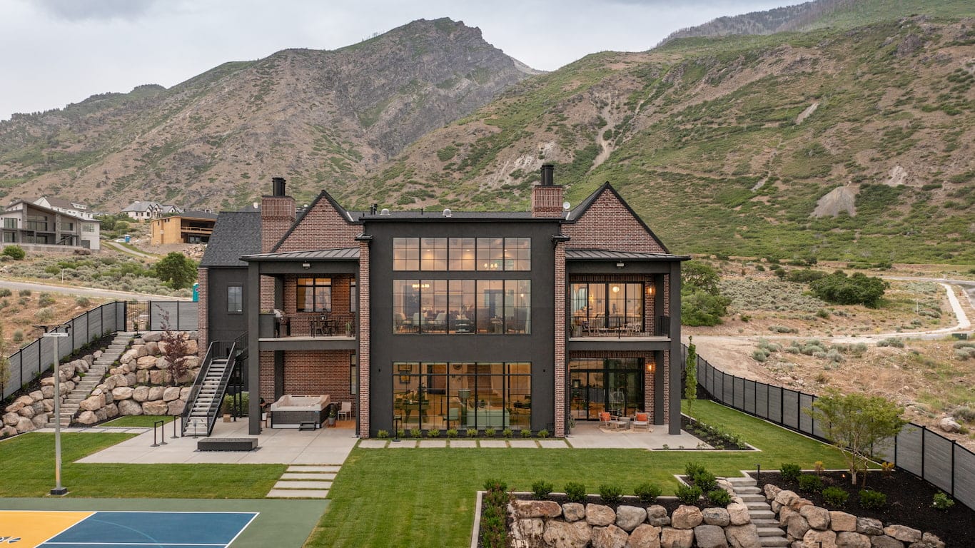 The exterior of a traditional home near the mountains features black windows and doors and a big backyard.