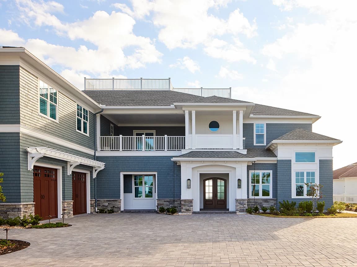 A modern coastal home with hurricane-resistant features, blue siding, white trim, and large windows.