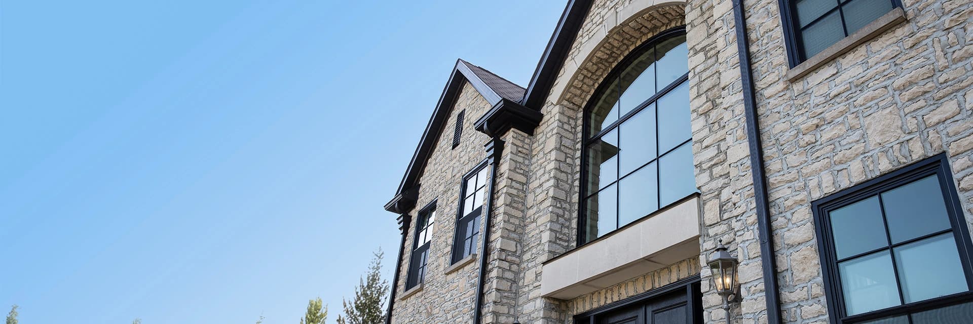 A close-up view of a stone home in Columbus, OH, featuring striking black-framed windows that add a modern touch to the classic architecture under a clear blue sky.