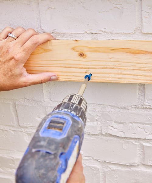 Using a screwdriver to attach a board to a home exterior that will be used to hang a window box.