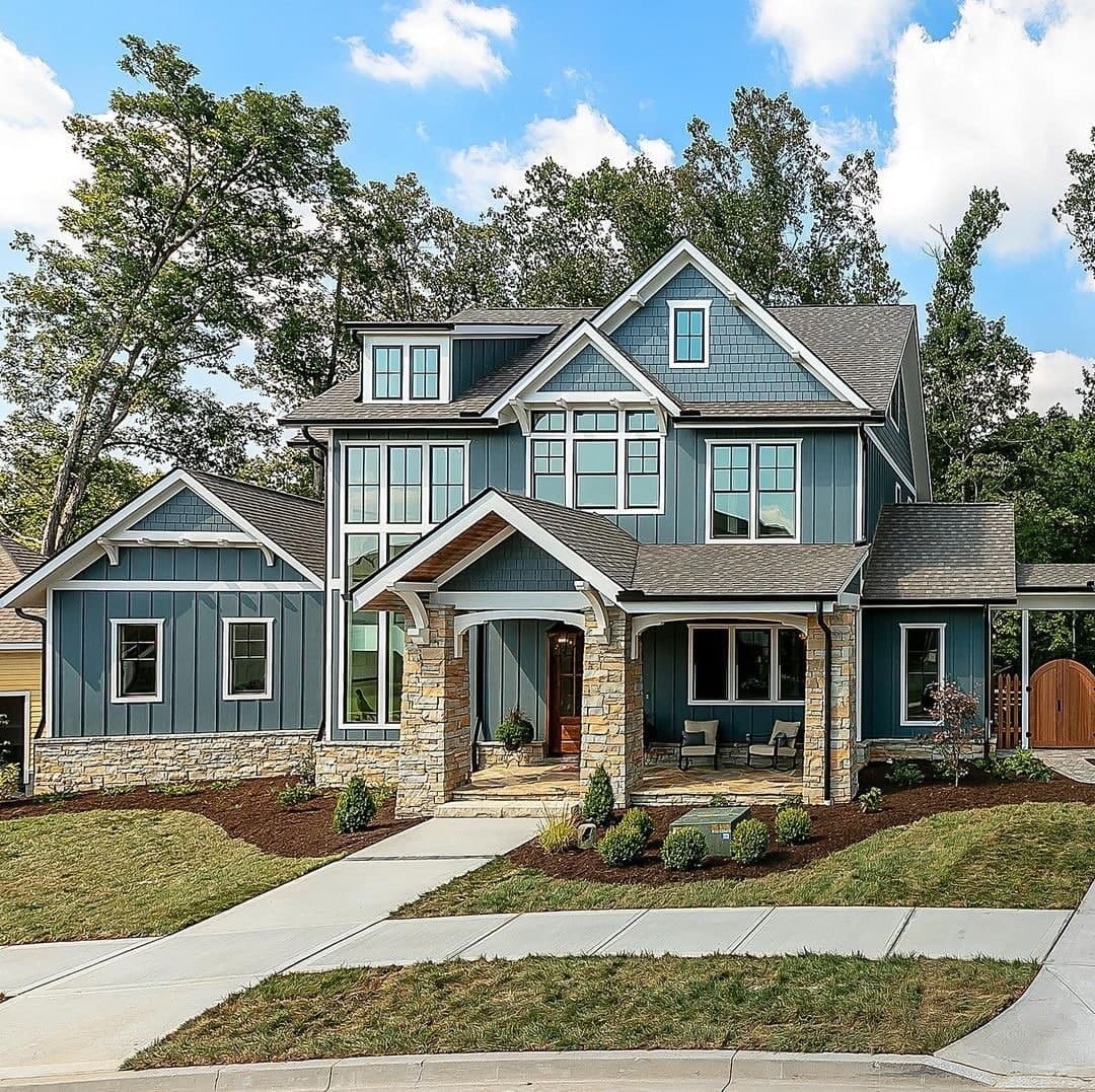 The exterior of a blue house has black windows with white trim.