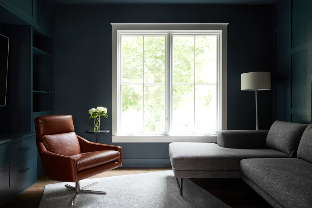 White Windows Contrast Dark Walls In Contemporary Design dark living room walls contrasts with two white casement windows and brown leather chair