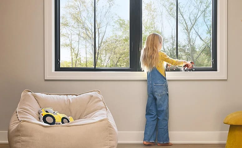 A child plays with toys by a large black fiberglass window in a bright, modern room.