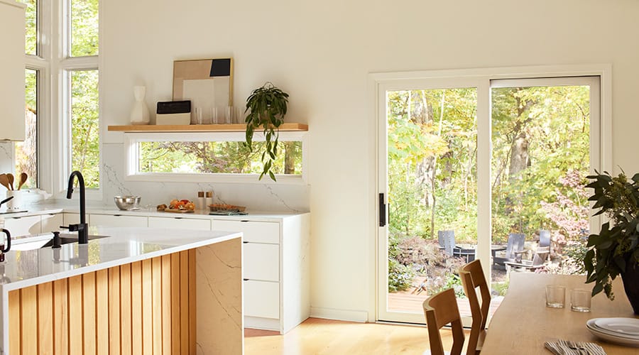 An all white kitchen and dining room features clerestory windows and a large white sliding patio door.