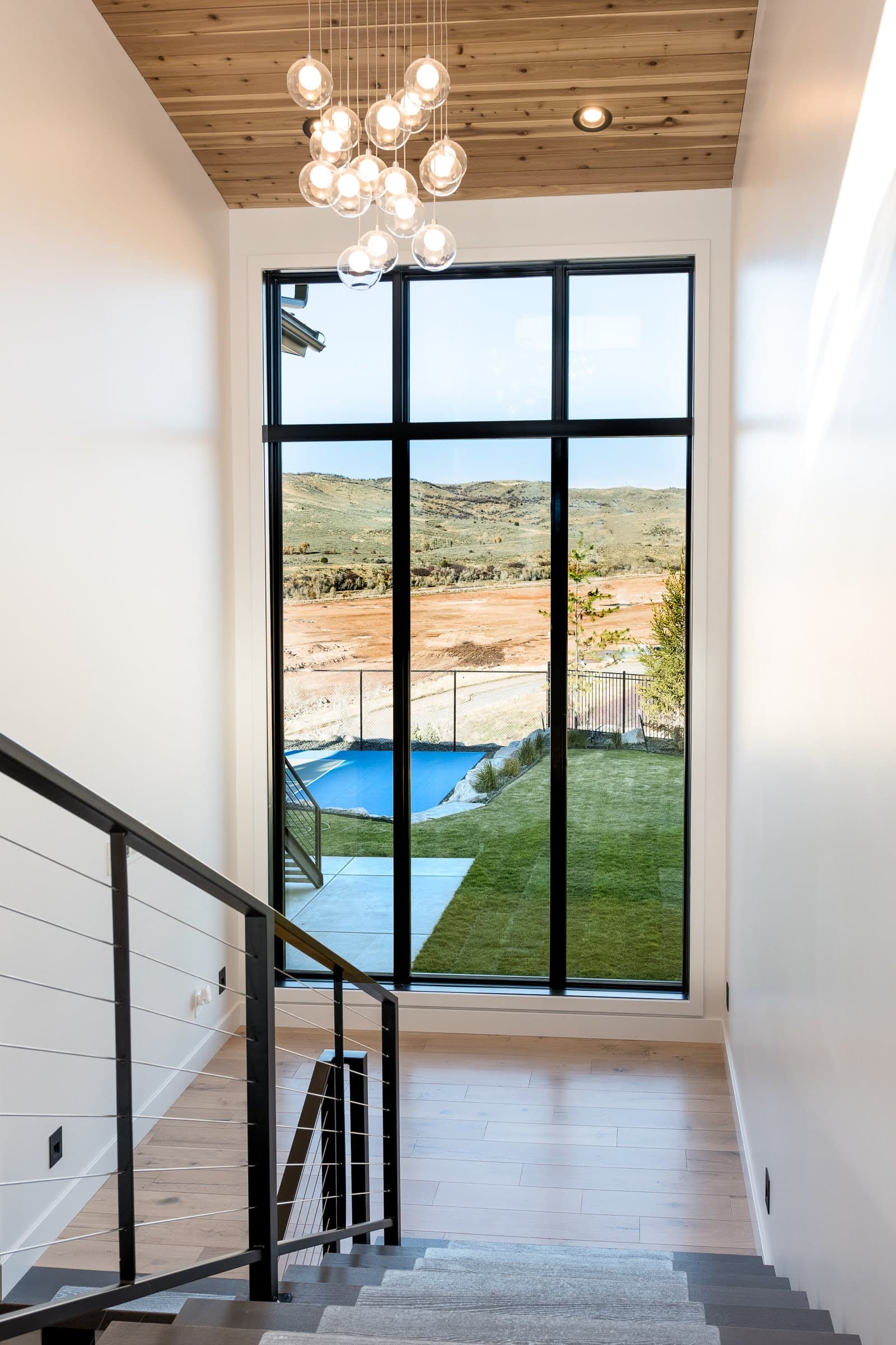 Floor-to-ceiling windows at the landing of a staircase overlook a Utah backyard.