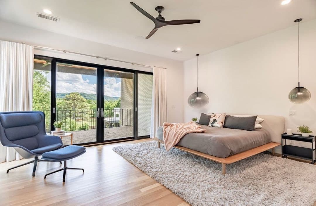 Black sliding patio doors in a white bedroom overlook the balcony and trees outside.