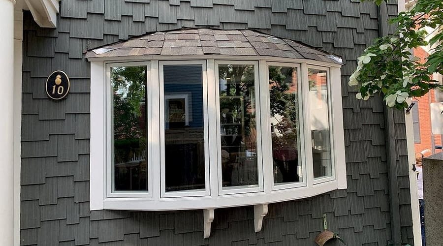 A bow window is comprised of five casement windows curving outward from the exterior of a gray home.
