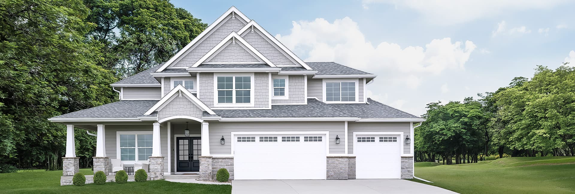 Modern two-story gray suburban house with three-car garage, covered front porch and landscaped lawn
