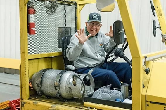 Smiling forklift operator in a yellow vehicle highlights diverse careers in logistics.