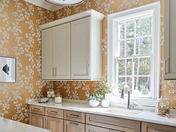 A traditional kitchen with yellow patterned wallpaper and a white window over the sink.