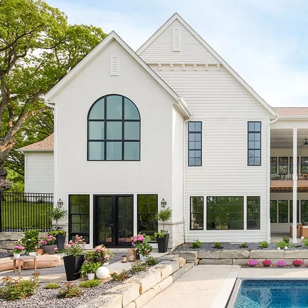 Modern white house with large black window grilles and a landscaped poolside garden.