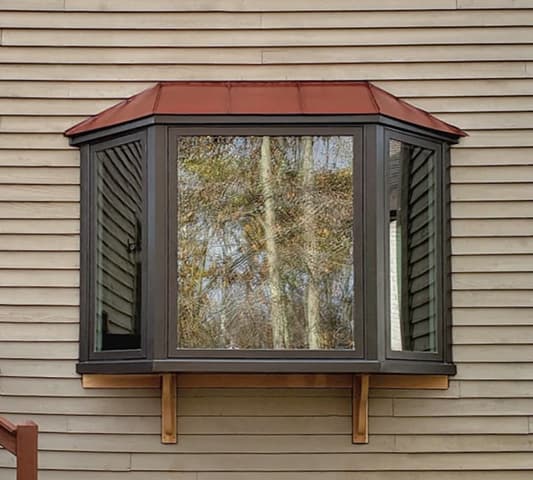 A black bay window with a copper roof extends beyond the exterior walls of a home with beige siding.