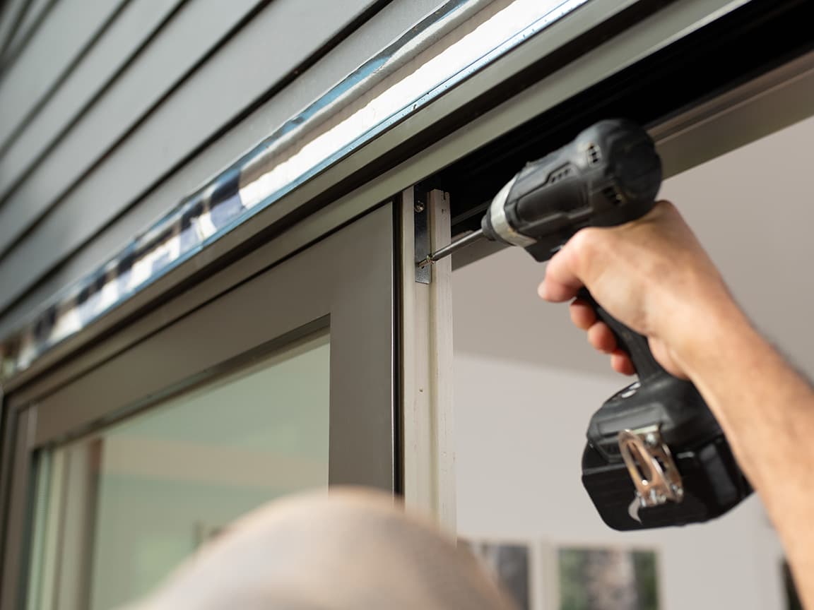 A person is using a drill to complete the installation of a brown sliding patio door.