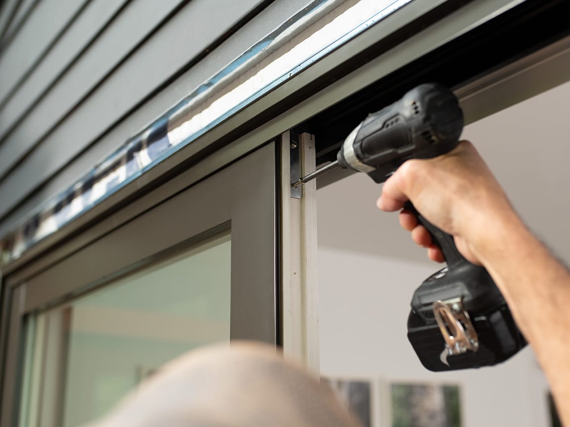 A person is using a drill to complete the installation of a brown sliding patio door.