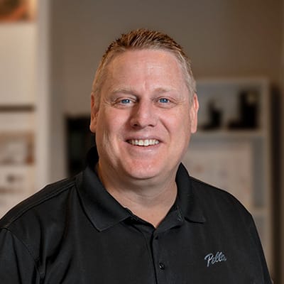 A man named Scott is wearing a black Pella shirt and smiling at the camera lens.