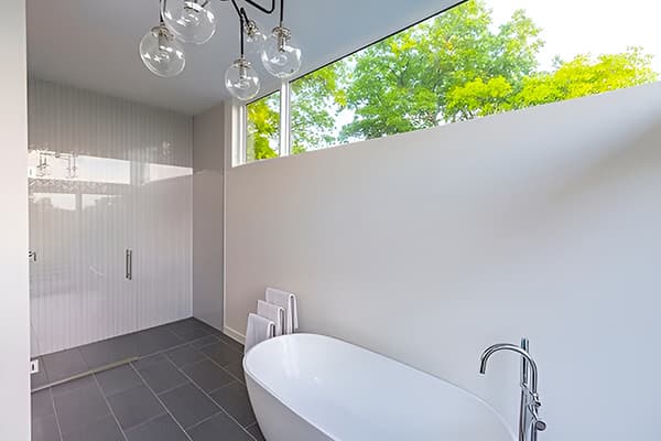 Bathroom Windows Placed High Let In Light & Maintain Privacy White modern bathroom with glass shower frame, white tub, and high fixed windows