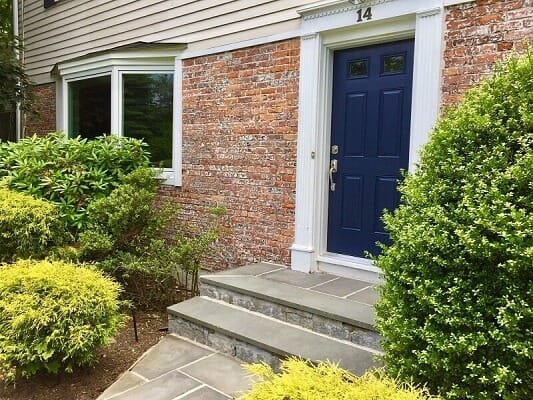 Navy Front Door Pops On Traditional Style Home Navy blue front door with white trim has large green bushes on either side