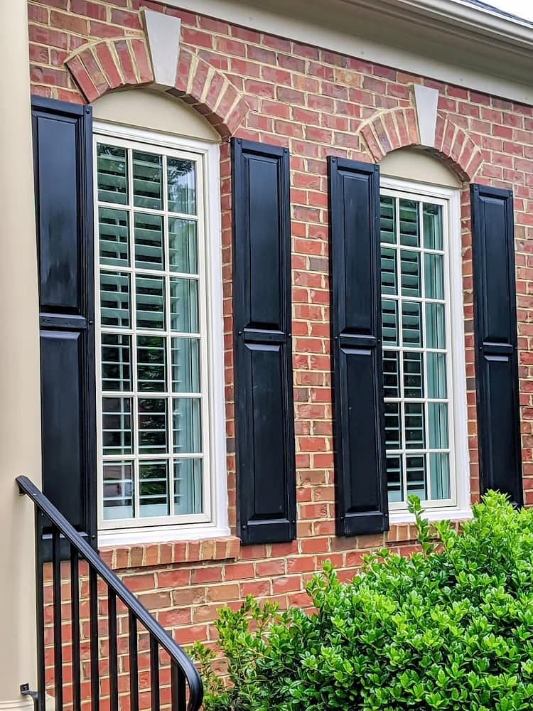 White windows with simple grilles and black shutters complete the exterior of a red brick home.
