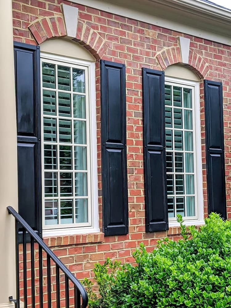 White windows with simple grilles and black shutters complete the exterior of a red brick home.