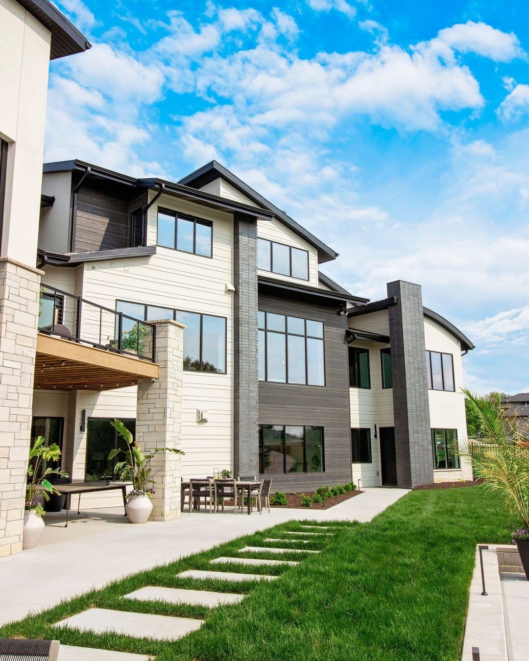 The exterior of a house features three levels of black windows, including a walkout basement that connects to the backyard patio.