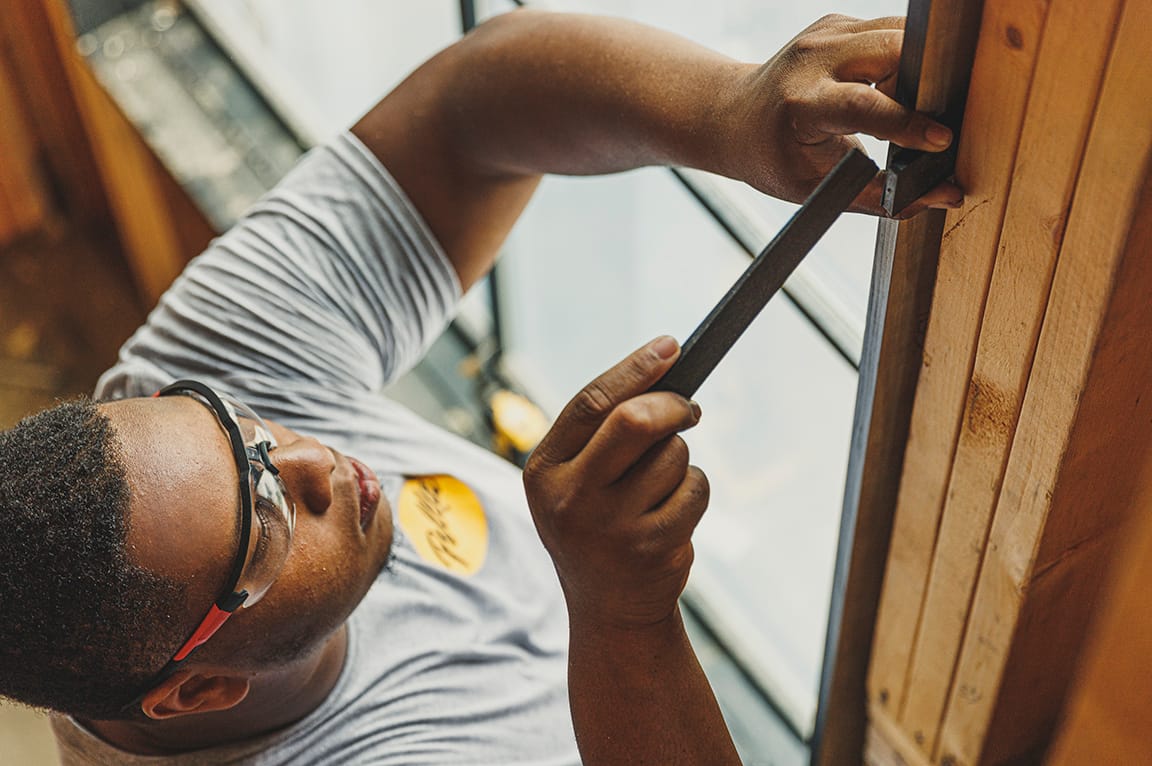 A man wearing safety glasses installs a replacement window using a tool, demonstrating replacing a replacement window.