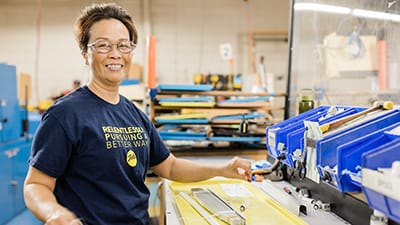 A woman is working in a manufacturing facility and enjoying her job.