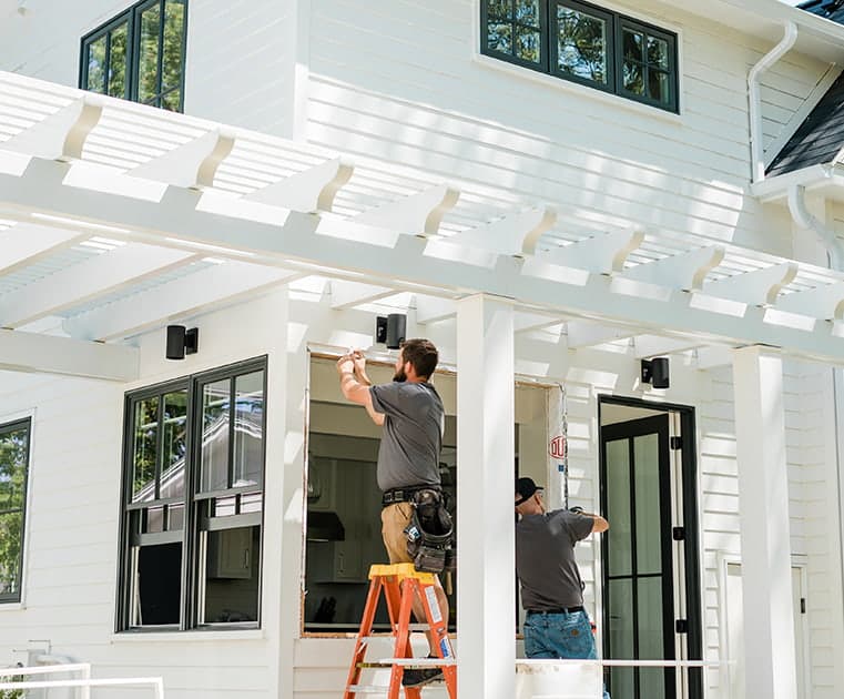 two contractors adding new windows to a farmhouse-style home