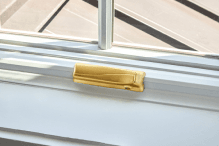 A white Pella casement window with the fold-away crank in a brushed gold finish.