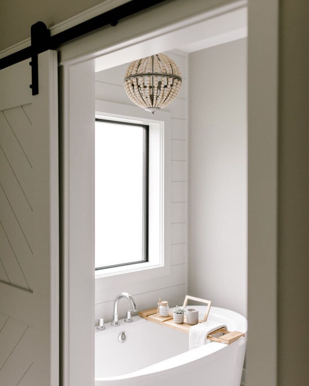 Fixed Window In Farmhouse Bathroom Lets In Natural Light freestanding bathroom tub with chandelier and large fixed window
