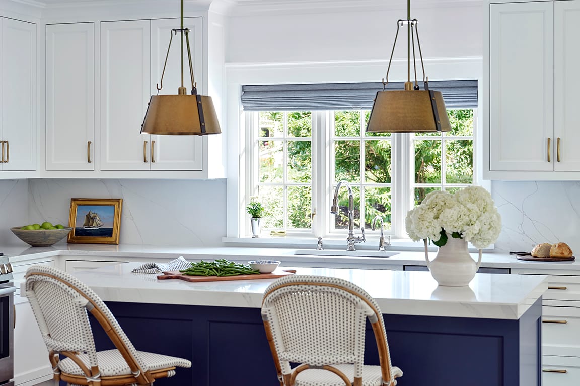 Large over-the sink windows complement a modern kitchen with white cabinets and a central island.
