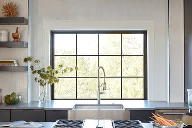 A modern kitchen featuring an over-the-sink window with a black frame, showcasing greenery and a sleek design.