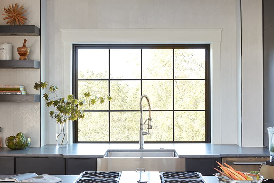 A modern kitchen featuring an over-the-sink window with a black frame, showcasing greenery and a sleek design.