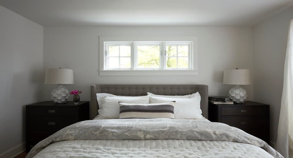 Pella Reserve Windows Crafted To Reproduce Historic Details Perfectly made bed with three small square windows directly above and nightstands on either side