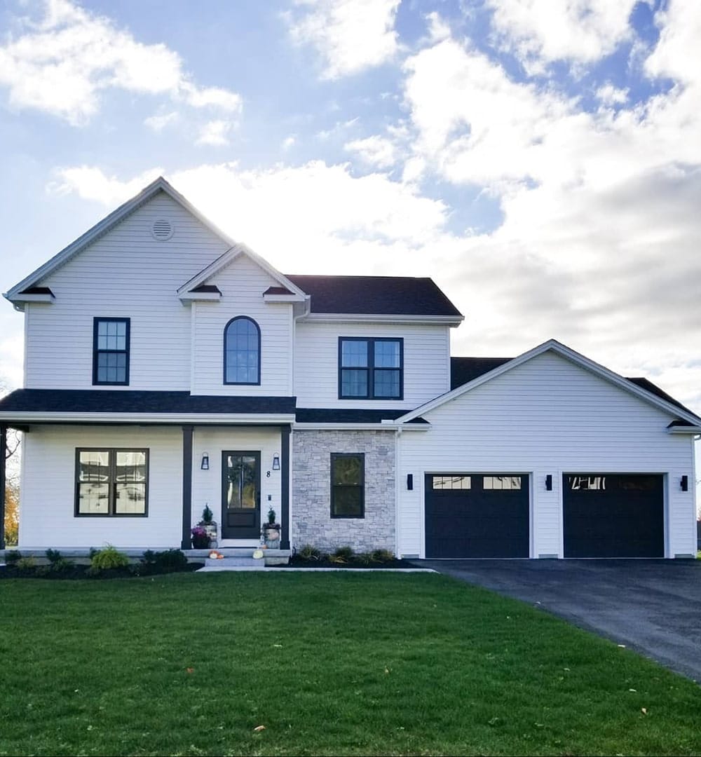 A white farmhouse exterior features black double-hung and picture windows, including a custom arch window over the front door.