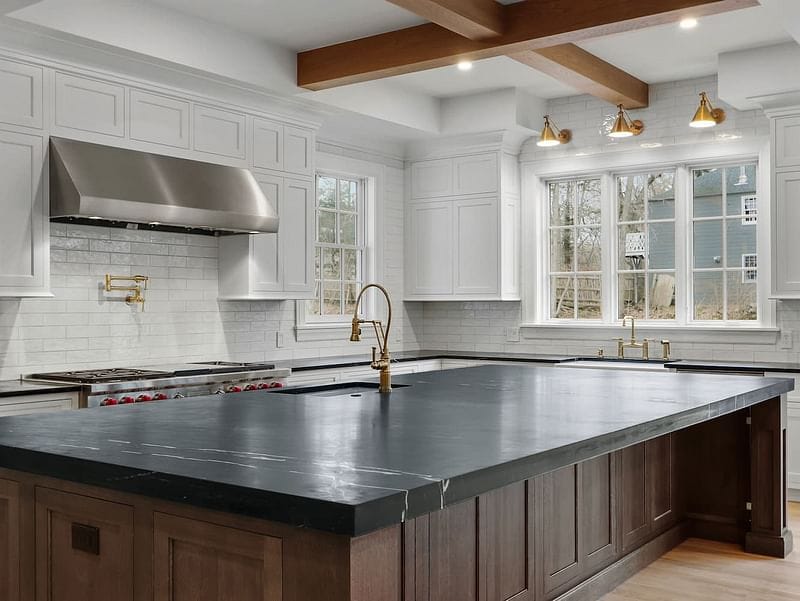 A large kitchen with white windows and a large black countertop.