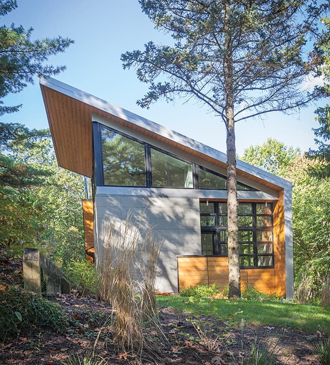 A mid-century modern home nestled in trees featuring a slanted room and triangle windows.