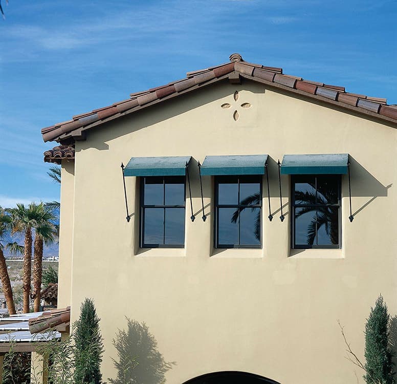 Three casement windows with fabric awnings on a second floor stucco home.