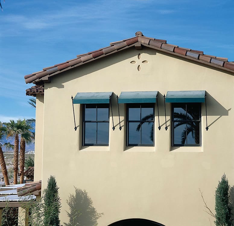 Three casement windows with fabric awnings on a second floor stucco home.