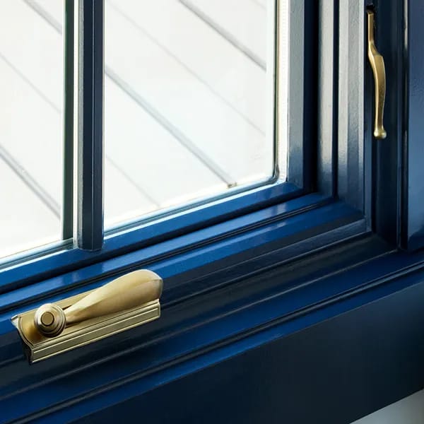 Close-up of a window frame in a custom color blue with brass hardware and clear glass.