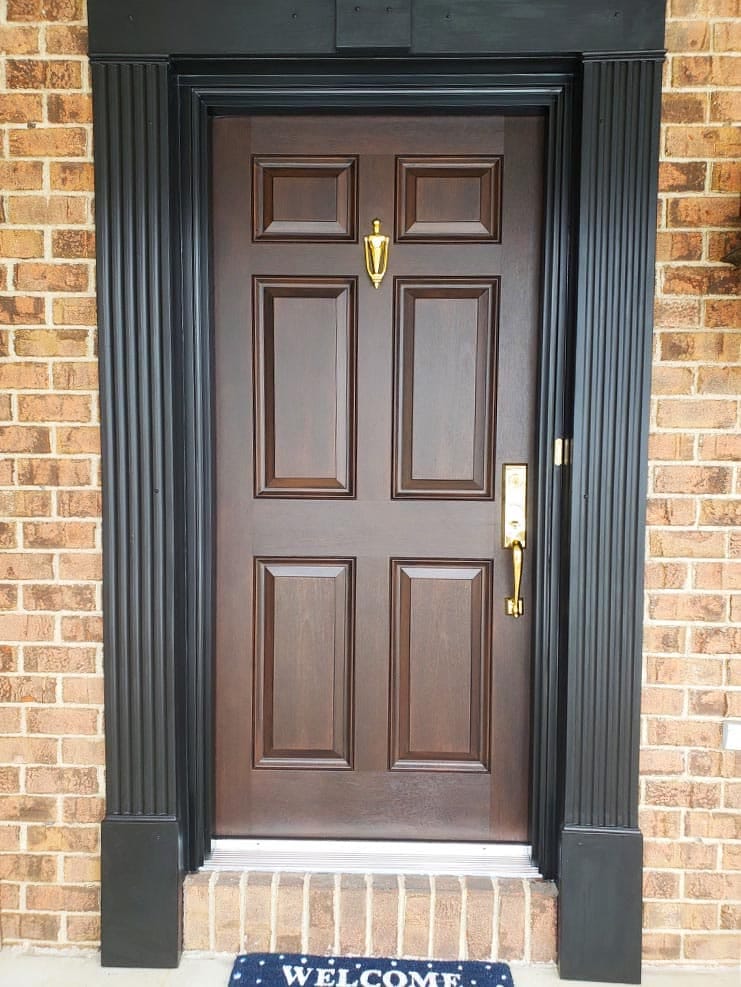 Brown Front Door Paired With Brass Hardware & Black Trim Brown front door with brass hardware and black trim on brick house