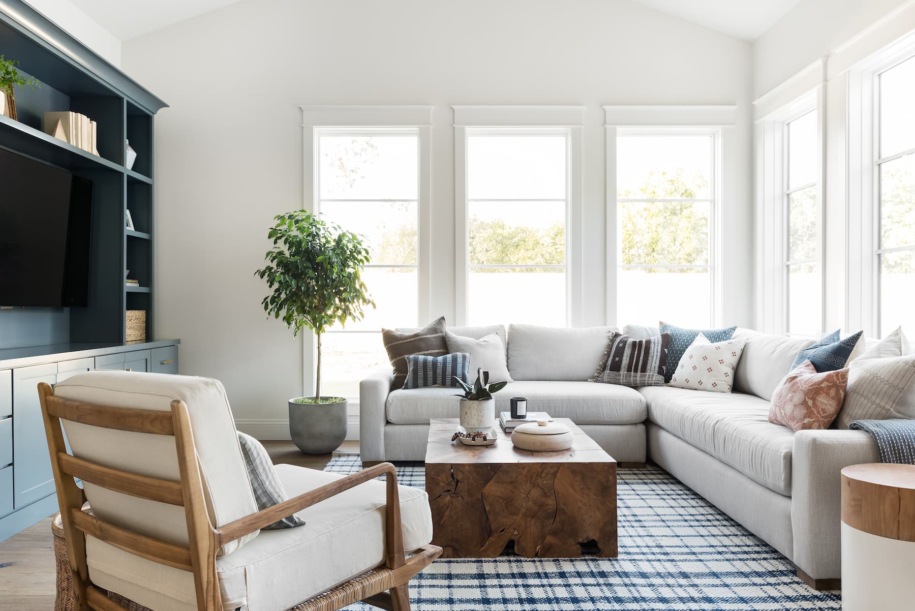 An Arizona living room has a sectional couch with blue accents and white picture windows lining the exterior walls behind the couch.