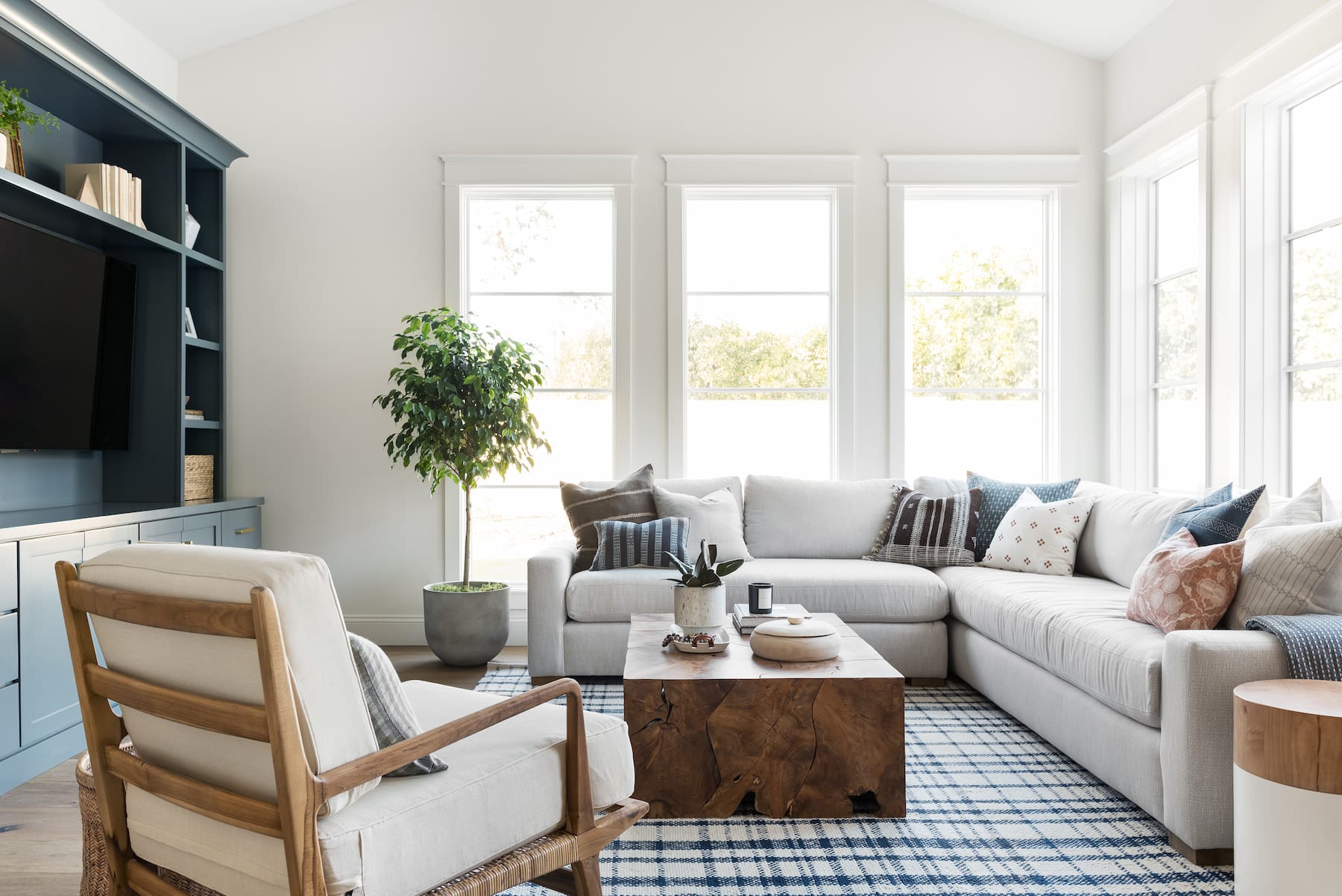 An Arizona living room has a sectional couch with blue accents and white picture windows lining the exterior walls behind the couch.