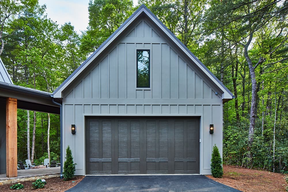 A large steel gray garage has an attic above with a tall single fixed window.