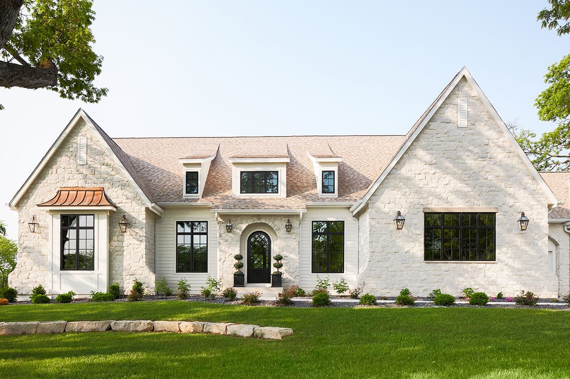 A modern home with stone exterior featuring black casement windows and a well-manicured lawn.