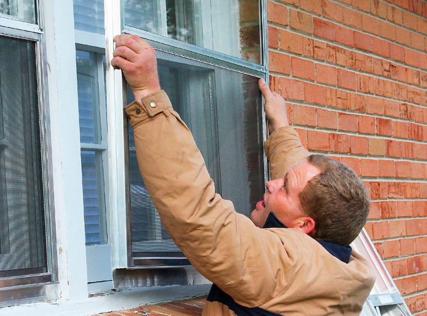 a homeowner installing a storm window on the exterior of a brick home