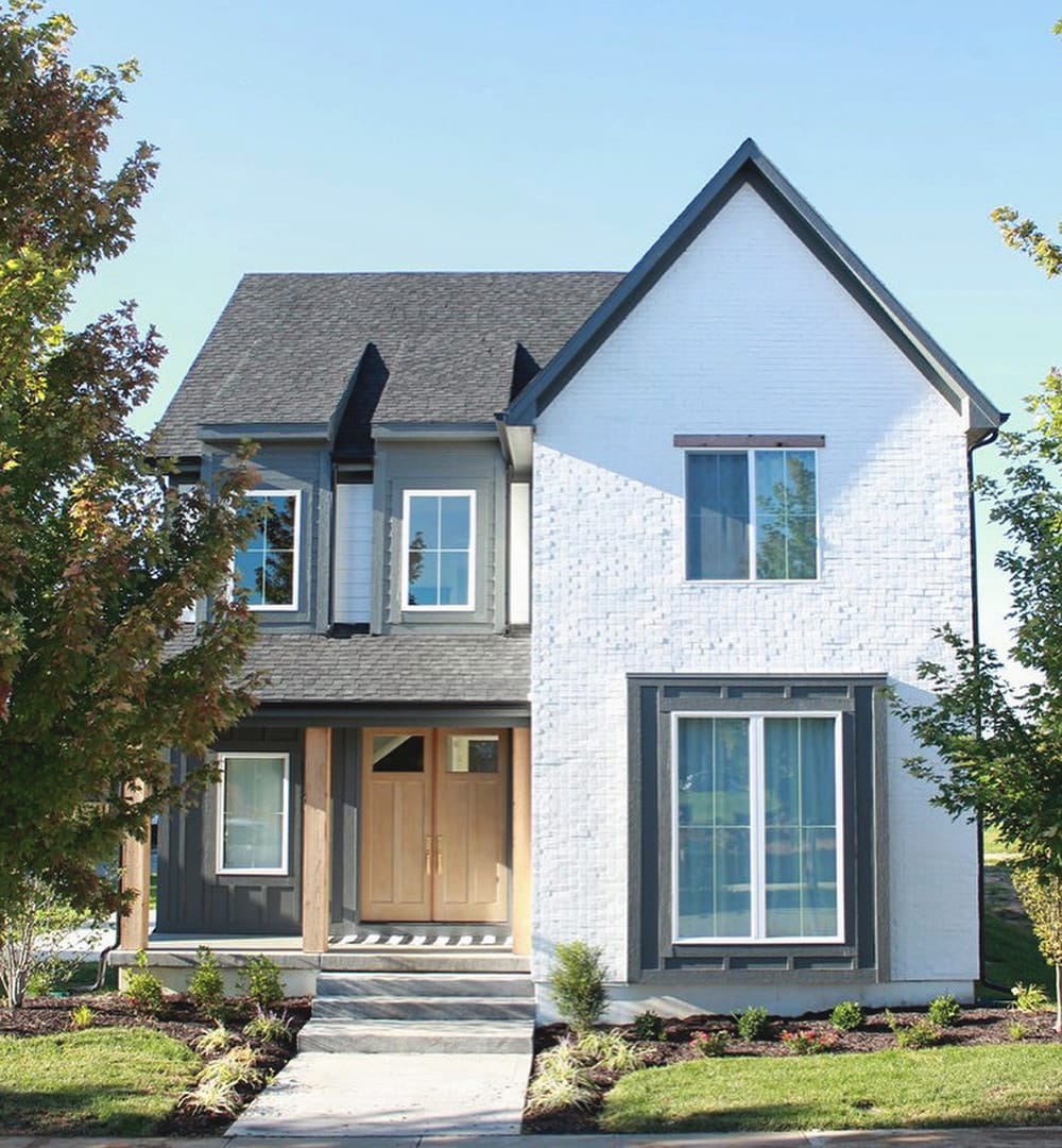 A small farmhouse style house features white windows and matching white brick, contrasting the gray siding.