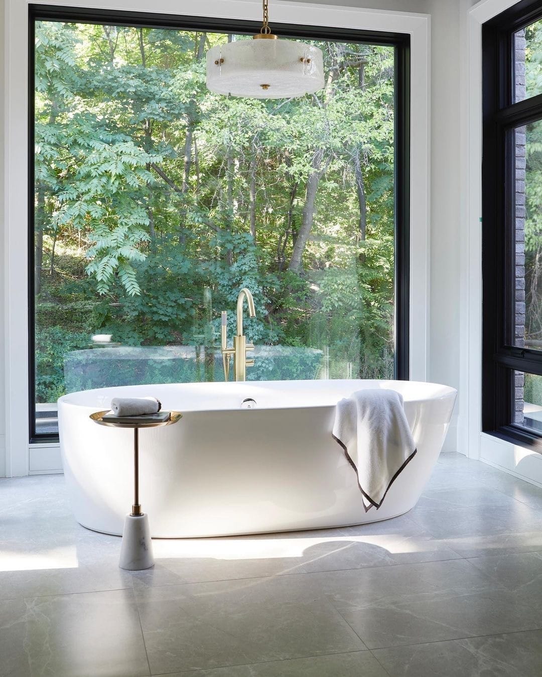 A floor-to-ceiling bathroom window sits behind a white bathtub.