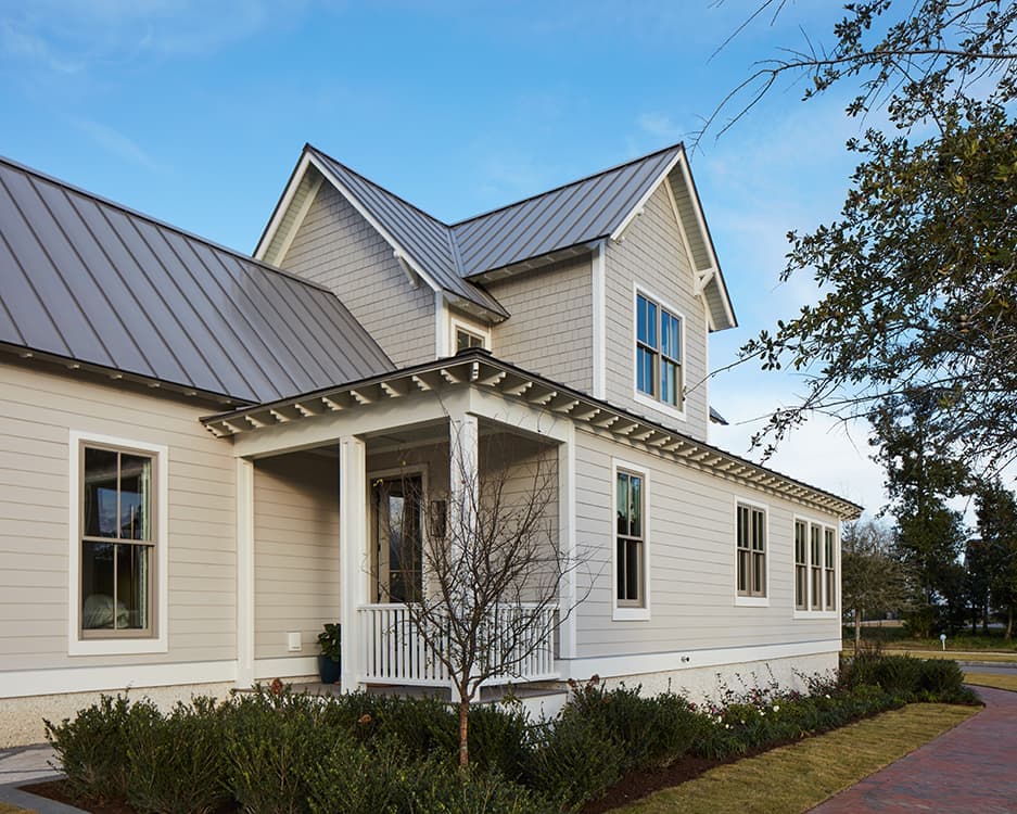 Two-story modern farmhouse exterior with light horizontal siding, metal gable roof, covered front porch, multiple windows and landscaped yard with brick walkway.