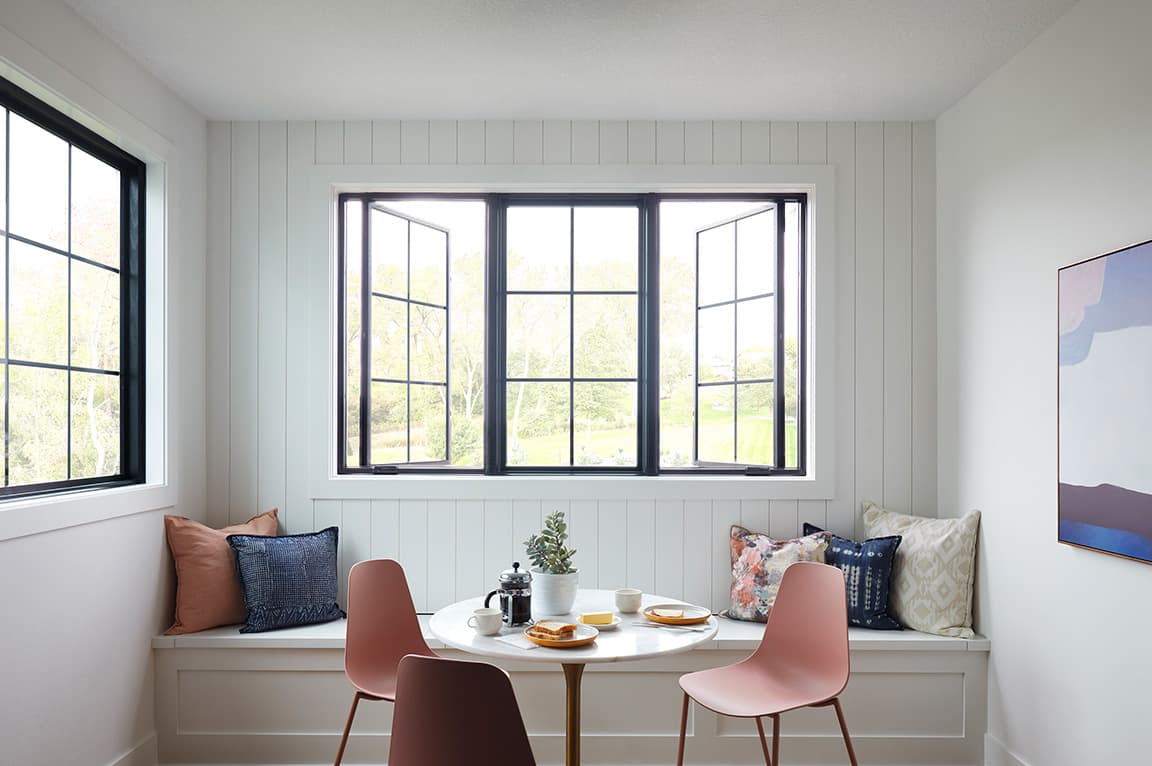 A modern dining area featuring a casement window with black frames, a round table, and stylish chairs.