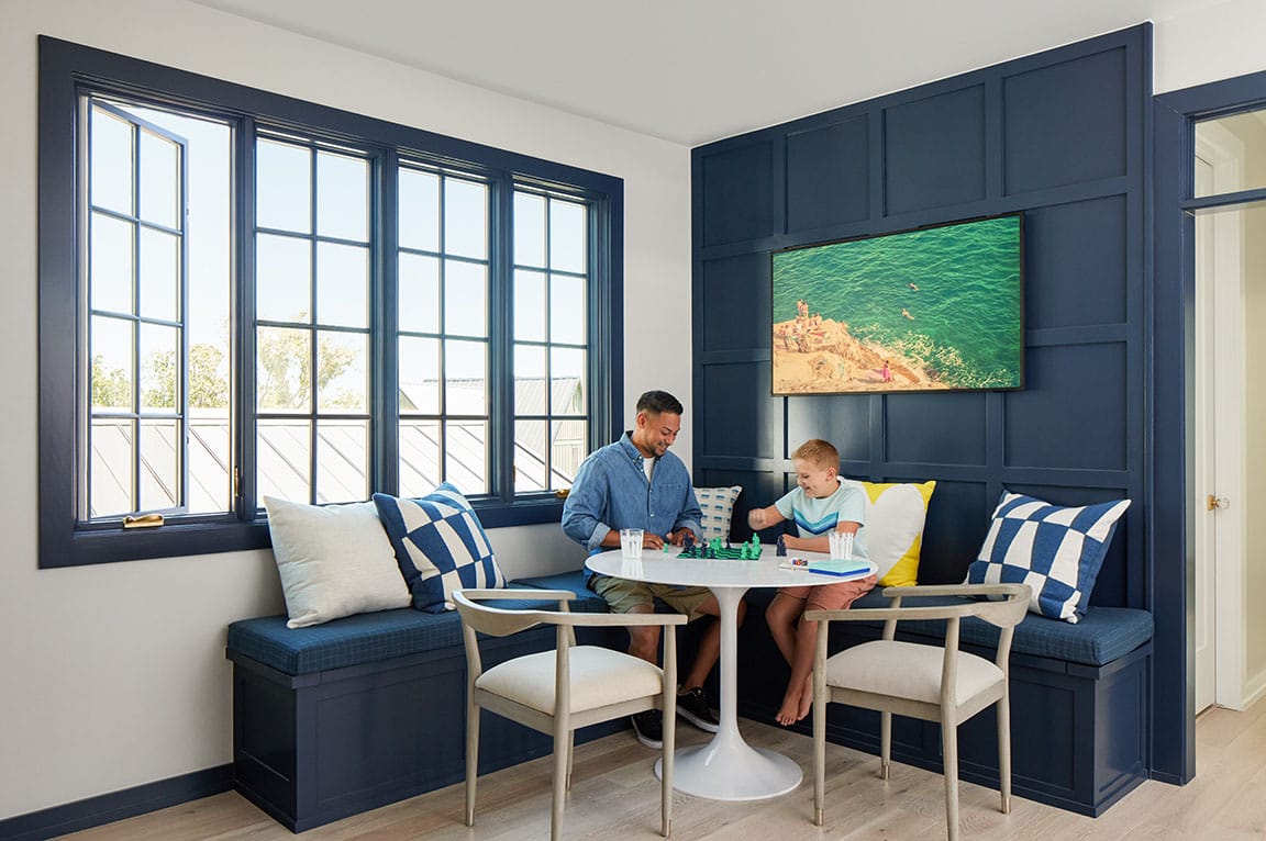 A modern living room with a blue casement window, featuring a family playing chess at a round table.